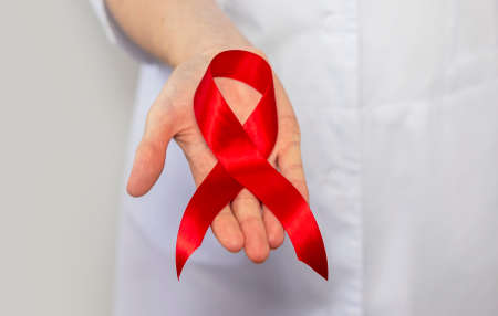 Red ribbon for aids and hiv world day support, close up. Hand of female doctor.