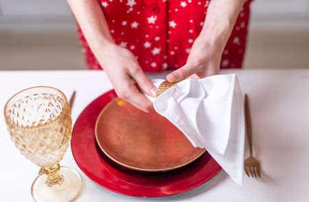 Female hands close up set the table for christmas, decorating it with white napkin, plates and wineglass, cutlery. Prepararion for festive dinner, top view.の写真素材