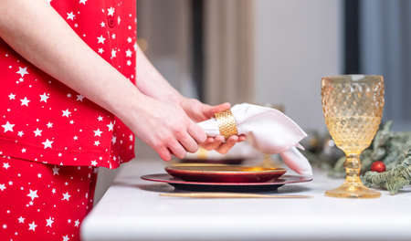 Female hands close up set the table for christmas, decorating it with white napkin, plates and...