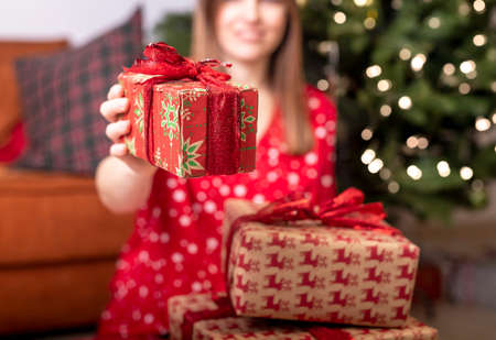 Cropped caucasuian woman holding or showing christams gift or present wrapped in paper with red ribbon and bow. Close up of a box.の写真素材