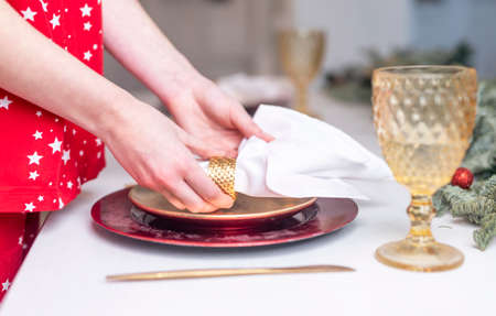 Female hands close up set the table for christmas, decorating it with white napkin, plates and wineglass, cutlery. Prepararion for festive dinner, side view.の写真素材