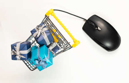 Online shopping concept. Trolley or cart full of wrapped gift boxes with computer mouse on white...