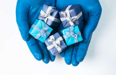 Hand in protective gloves holding small wrapped gifts over white background.の写真素材