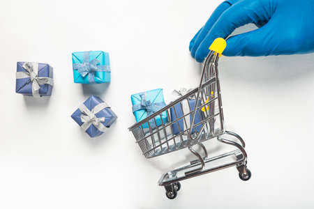 Shopping cart or trolley full of scattered gift boxes rolled by hand in glove. Trolley with presents for christmas isolated on white background, side view.の写真素材