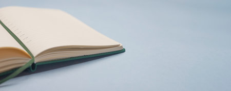 Open notebook on blue office desk, side view, close up. Banner with copy space or place for text