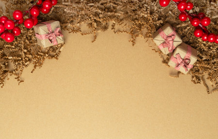Eco friendly Christmas background with wrapped gifts in craft paper, ribbons, viburnum at top and place for text or copy space on brown paper.の写真素材