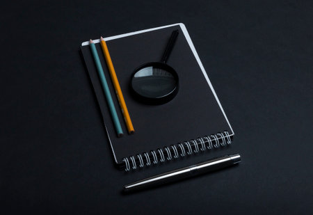 Notebook with pen, pencil and magnifying glass on black background.の写真素材