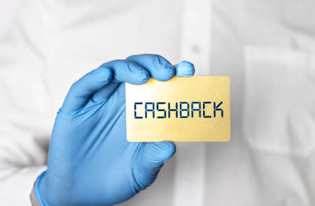 Cashback word on golden bank card in hands of man in protective gloves.の写真素材