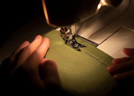 Close up of women hands at textile under needle of sewing machine. Slow fashion concept.の写真素材