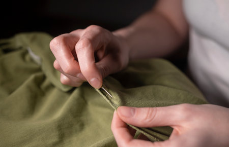 Female hands with needle and thread repairing clothes, close up.の写真素材
