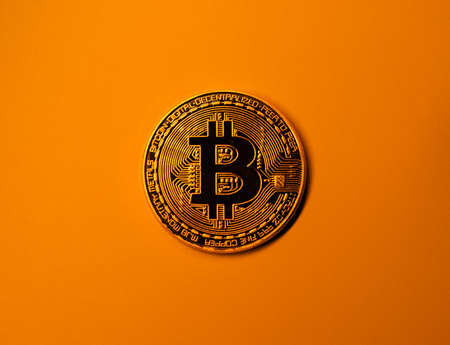 Golden bitcoin coin on yellow monochrome background.