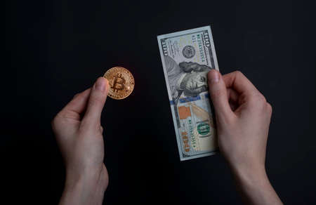 Hands holding bitcoin and banknote of us dollar on black background.