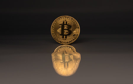 Golden coin of bitcoin on black gray reflective background with reflection.