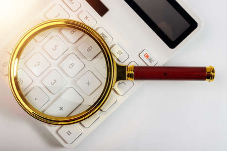 Magnifying glass on white calculator, analysis and accounting concept.の写真素材