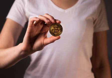 Golden coin of BTC or bitcoin held bu female hand.