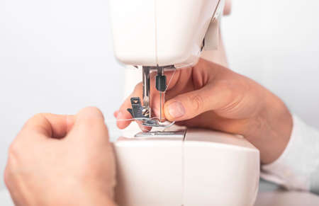 Male hands adjusting or setting sewing machine, close up.