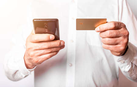 Male hands holding mobile phone and plastic card, entering data to bank app to pay online. Front...