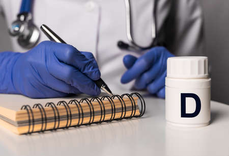 Doctor writing prescriptions for D vitamib close up. Medical and pharmacy concept.