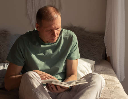 Mature man reading book. Mature person on bed restingの写真素材
