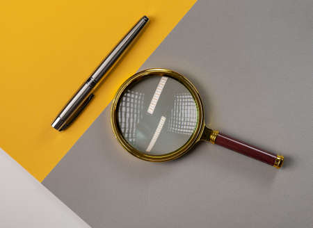 Magnifier and pen on gray and yellow background.の写真素材
