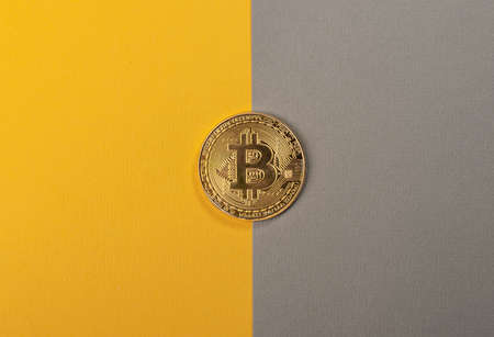 Shining bitcoin coin on trendy yellow and gray background.