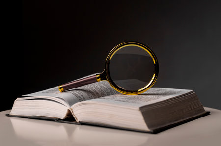 Open book closeup with turning pages and magnifying loupe. Textbook in hard cover on table. Studying and research concept.