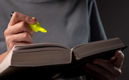 Female student hands holding yellow highlighter and reading book or textbook, making notes,...