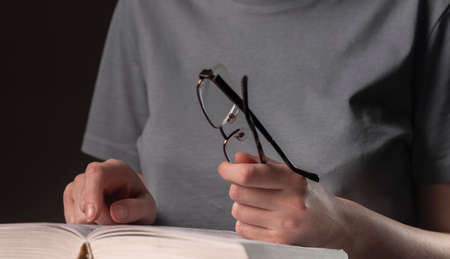 Female student hands close up, holding eyeglasses and book or textbook, searching for information and reading at night.の写真素材
