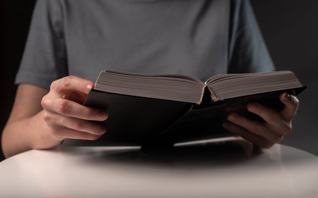 Female hands close up, holding and reading book or textbook in hardcover at night.