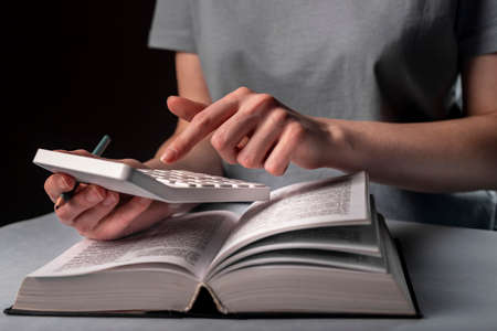 Female hands calculating finances on calculator with financial book or code at night.の写真素材