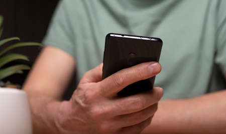 Man using mobile phone close up. Male hands at wooden table with plant holding smartphone and...