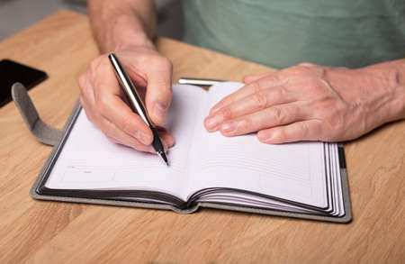 Male hands taking notes, writing plans in notebook or planner. Planning in schedule diary, close up....