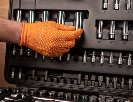 Male hand in building glove with socket ratchet handle, taken from toolbox. Industrial metal tool, close up on wooden background.の写真素材