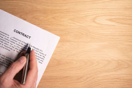 Male hand over legal contract with copy space for text on wooden desk, top view.