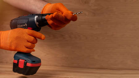 Male hand in building gloves holding professional cordless drill tool or machine for using in repair...
