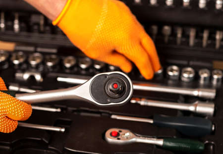 Male hand in building glove with socket ratchet handle taking from repair suitcase. Industrial metal...