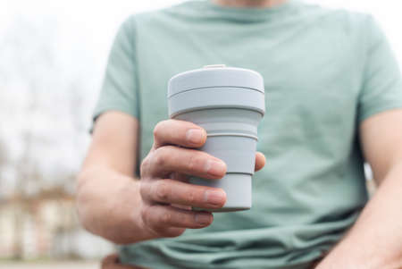 Collapsible cup for takeaway coffee or tea. Male hand with sustainable silicon mug. Eco lifestyle.の写真素材