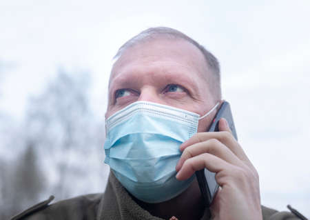 Mature man in face mask talking on mobile phone, close up. Modern after covid lifestyle.の写真素材
