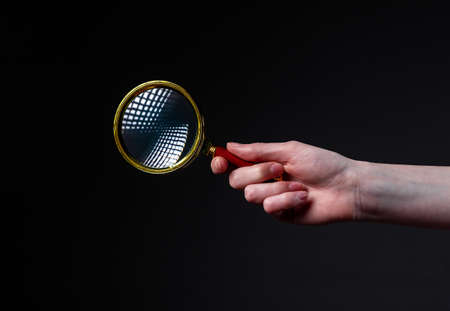 Magnifier or loupe in woman hand on black background. Concept of searching and studying.