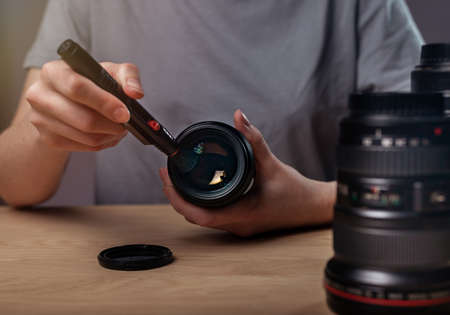 Female hands cleaning camera lens with black professional brush, closeup, removing dust and dirt.の写真素材