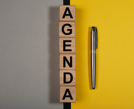 Agenda word on wooden cubes on yellow and gray background.の写真素材