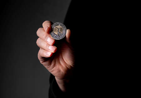 NEO silver coin in male hand over gray black background.