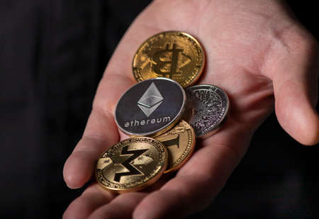 Shiny silver and gold coins of cryptocurrency in male hand palm over black background, close up....