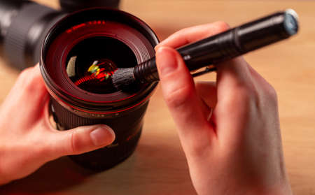 Female hands close up cleaning camera lens with black professional brush, closeup, removing dust with lenspen.の写真素材