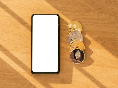 Crypto currency investing application mock up on mobile phone screen, bitcoin, ethereum on wooden...
