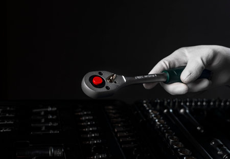 Male hand closeup in white glove with metal socket ratchet handle. Industrial steel tool, close up on black dark background over toolbox.の写真素材