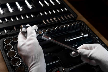Repairman hands closeup in white gloves holding metal handle extension tool over dark background...
