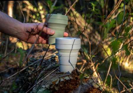 Eco-friendly reusable silicone coffee cup in forest taken by male hand among green plants and trees. Eco lifestyle. Beautiful daylight and shadows.の写真素材