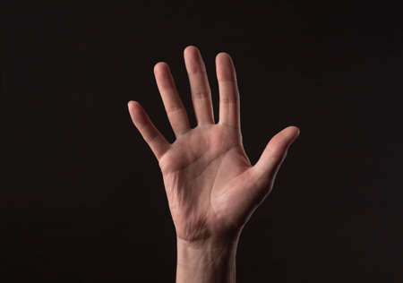 Male hand palm gesturing hello or hi over black background. greeting gesture.
