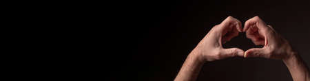 Heart-shaped male hands as peace and hope symbol over black background with copy space for text.の写真素材